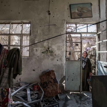 An older woman stands in the doorway of a destroyed home