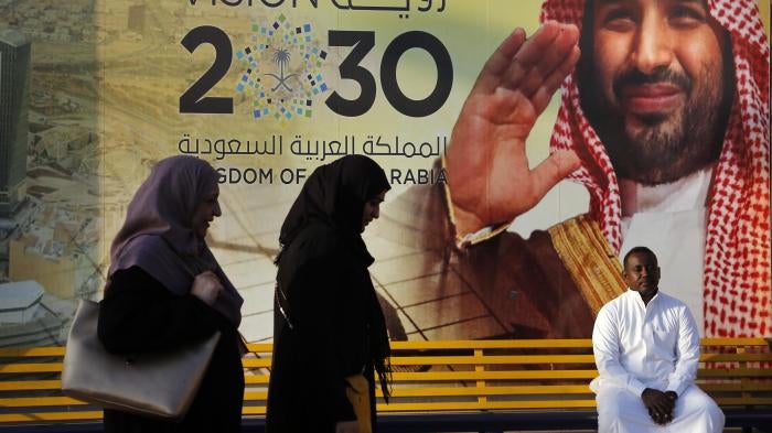 People walk past a Vision 2030 banner showing Saudi Crown Prince Mohammed bin Salman.