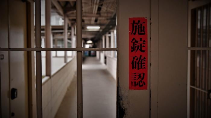 A sign in Japanese reads "check door lock" on a gate inside Tochigi prison