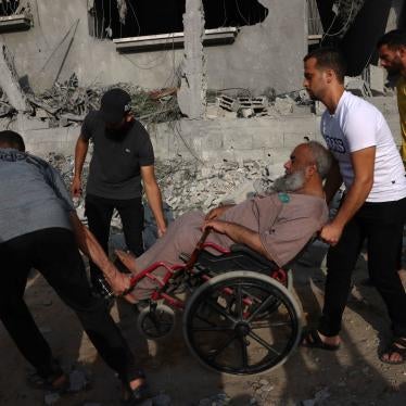 Three men help a man in a wheelchair move amid the rubble and destruction in the southern Gaza Strip on October 22, 2023. 