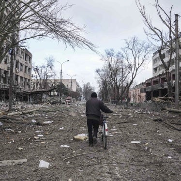 A cyclist walks down a damaged road with destroyed buildings on either side