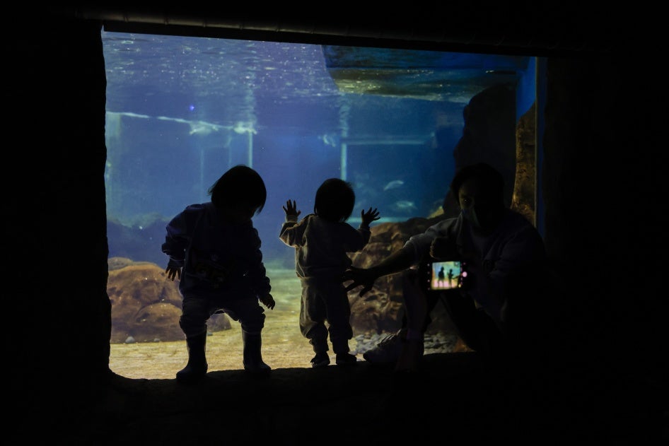 Two young children look at fish as an adult takes their photo at Sea Life Sydney Aquarium, Sydney, Australia, October 14, 2021.